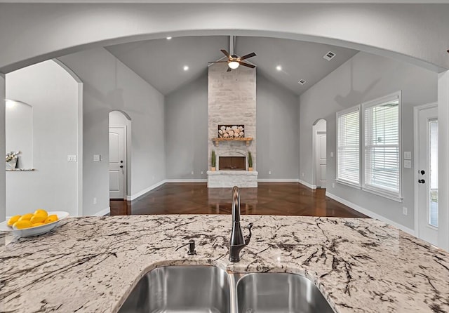 kitchen with a fireplace, light stone countertops, sink, and vaulted ceiling