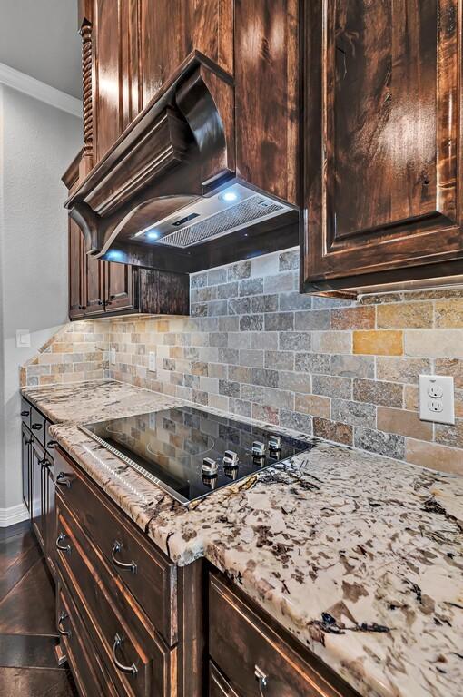 kitchen featuring black electric stovetop, backsplash, premium range hood, and dark brown cabinetry