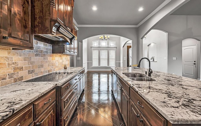 kitchen with light stone countertops, black electric cooktop, crown molding, sink, and a notable chandelier