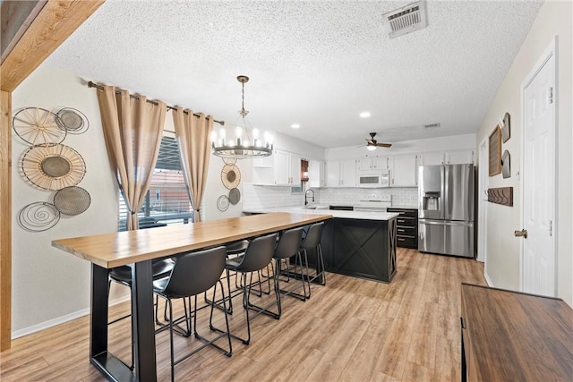 kitchen with ceiling fan with notable chandelier, white cabinets, decorative light fixtures, sink, and stainless steel fridge