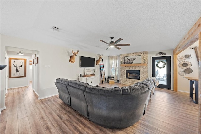 living room featuring ceiling fan, wood-type flooring, a textured ceiling, and a fireplace