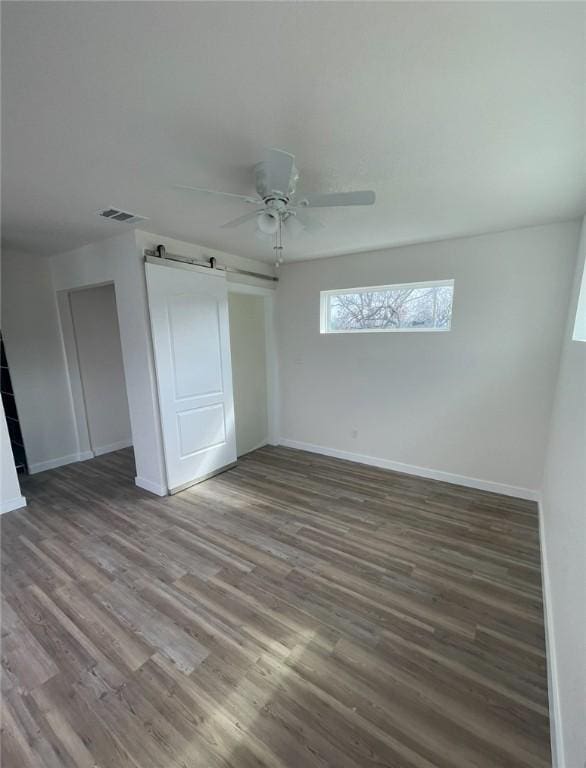 unfurnished bedroom with hardwood / wood-style floors, a barn door, and ceiling fan