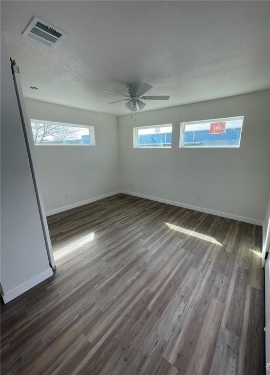 empty room with a barn door, dark hardwood / wood-style floors, a textured ceiling, and ceiling fan