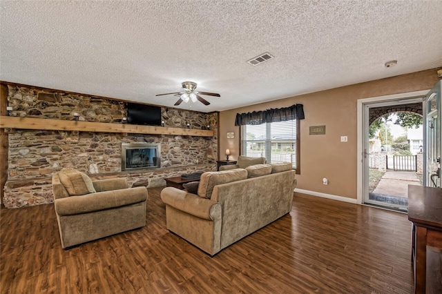 living room featuring a textured ceiling, a stone fireplace, ceiling fan, and dark hardwood / wood-style floors