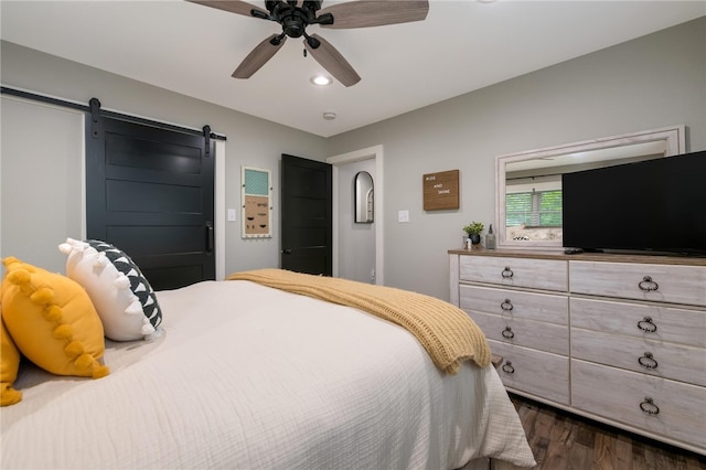 bedroom with a barn door, ceiling fan, and dark wood-type flooring