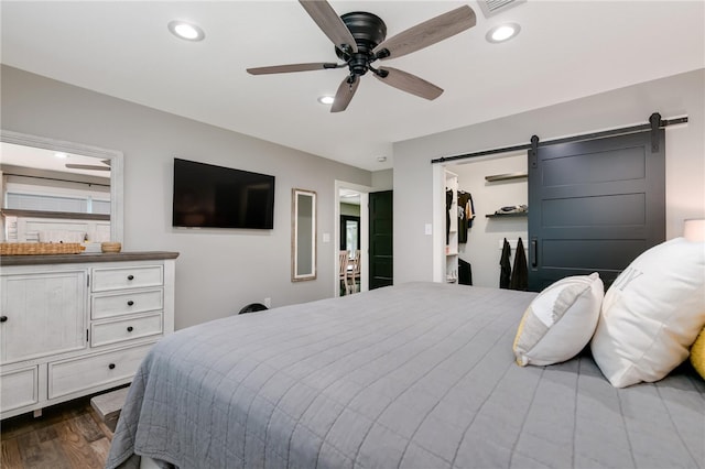 bedroom featuring dark hardwood / wood-style flooring, ceiling fan, a barn door, a spacious closet, and a closet