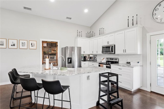 kitchen with a breakfast bar, a center island with sink, white cabinets, and appliances with stainless steel finishes