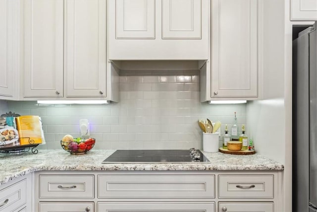 kitchen featuring tasteful backsplash, white cabinetry, black electric stovetop, and light stone counters