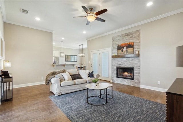 living room with dark hardwood / wood-style floors, ceiling fan, a stone fireplace, and crown molding