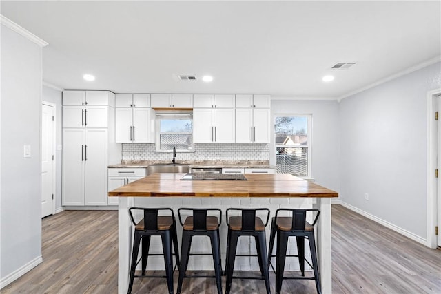 kitchen with a breakfast bar, white cabinets, sink, a kitchen island, and butcher block counters