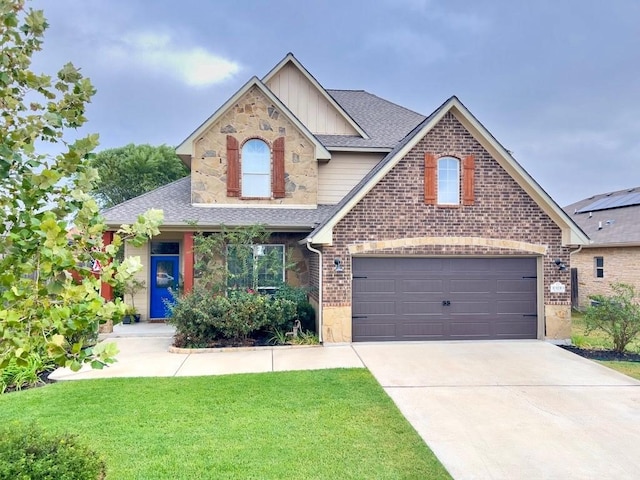 view of front facade with driveway, a shingled roof, stone siding, a front yard, and brick siding