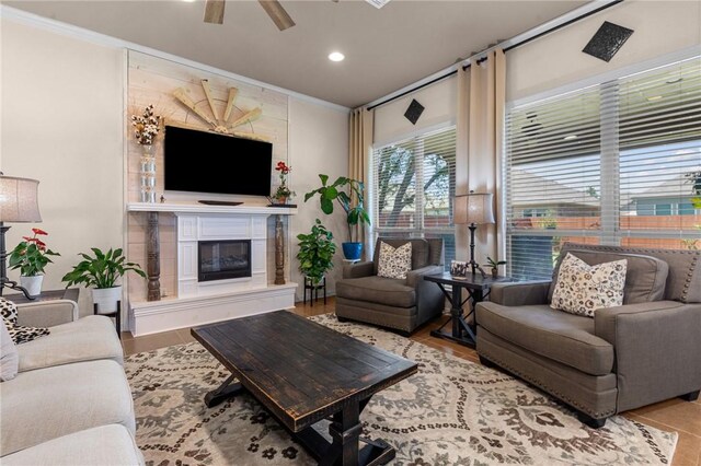 living room with ornamental molding, a glass covered fireplace, and a ceiling fan