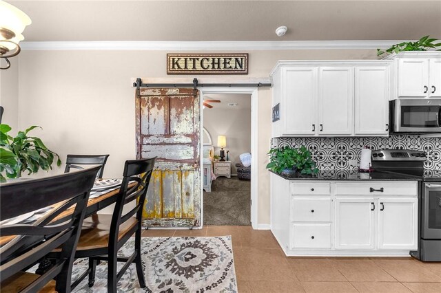 kitchen featuring a barn door, stainless steel appliances, white cabinets, ornamental molding, and dark countertops