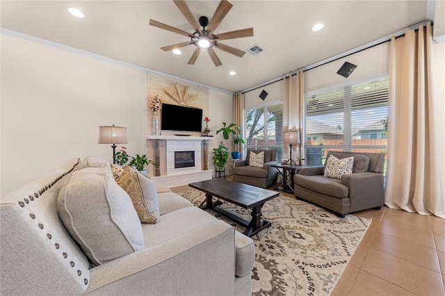 living area with light tile patterned floors, visible vents, a glass covered fireplace, crown molding, and recessed lighting