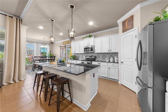 kitchen with a center island with sink, stainless steel appliances, crown molding, white cabinetry, and pendant lighting