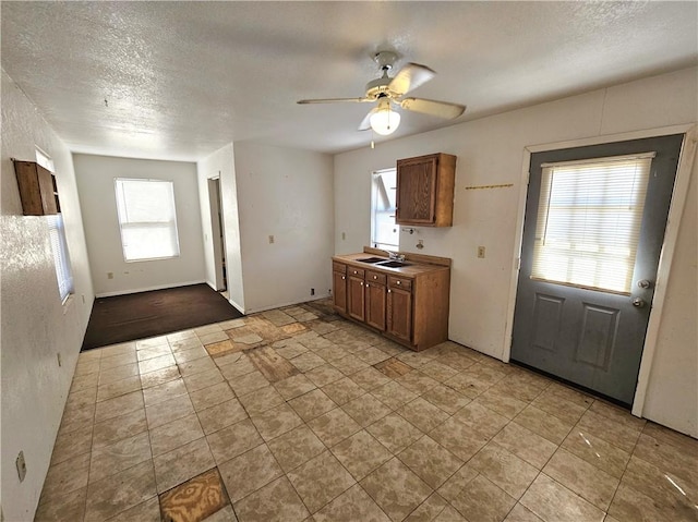 kitchen featuring a sink, brown cabinets, a textured ceiling, and a ceiling fan