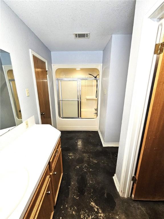 full bathroom featuring vanity, unfinished concrete floors, visible vents, a shower with shower door, and a textured ceiling