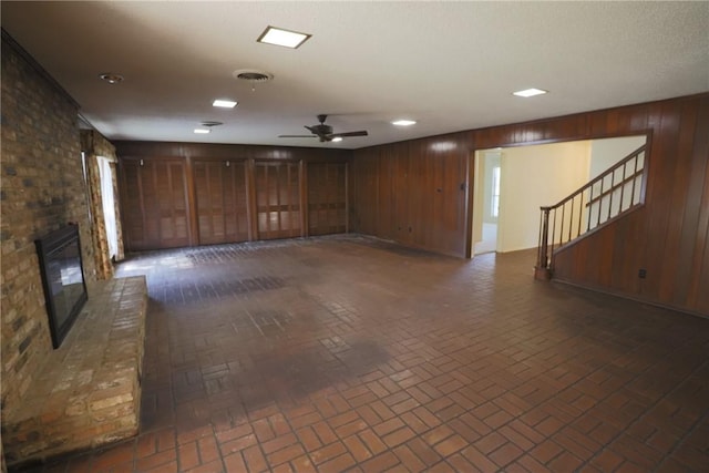 unfurnished living room featuring ceiling fan, wood walls, and a fireplace