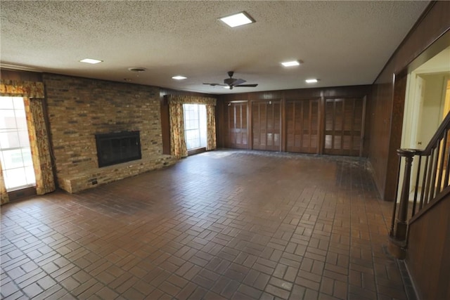 unfurnished living room with a textured ceiling, plenty of natural light, ceiling fan, and a fireplace