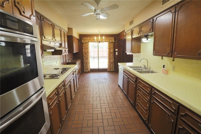 kitchen featuring backsplash, ceiling fan with notable chandelier, sink, appliances with stainless steel finishes, and decorative light fixtures