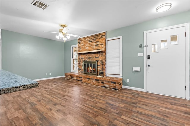 unfurnished living room featuring visible vents, baseboards, ceiling fan, wood finished floors, and a brick fireplace