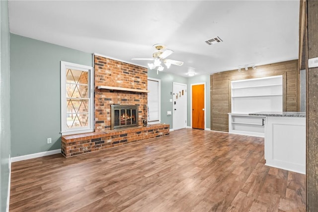 unfurnished living room with a fireplace, wood finished floors, visible vents, and baseboards