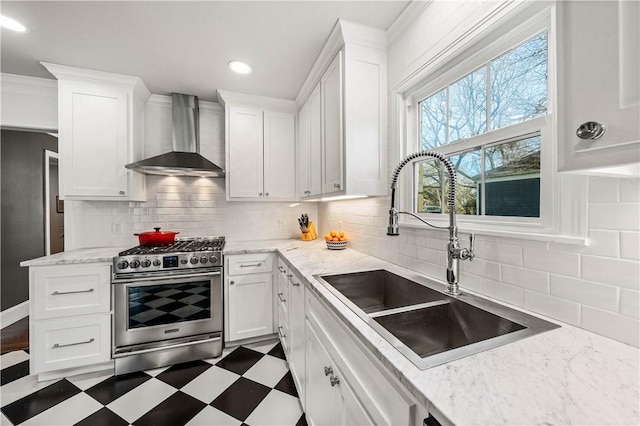 kitchen with white cabinets, sink, stainless steel stove, and wall chimney range hood