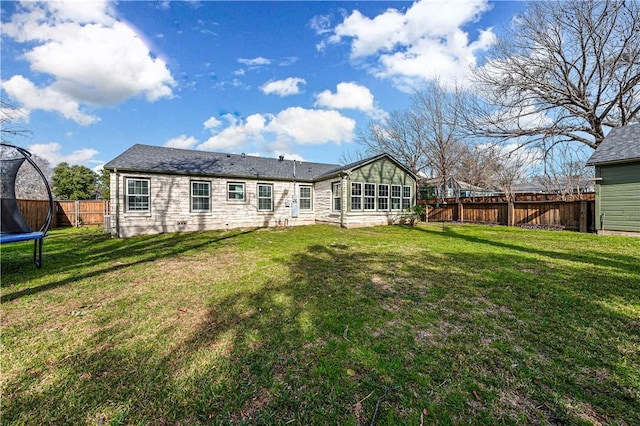 rear view of property with a trampoline and a lawn