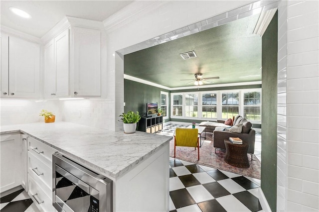 kitchen featuring light stone counters, stainless steel microwave, white cabinetry, and backsplash