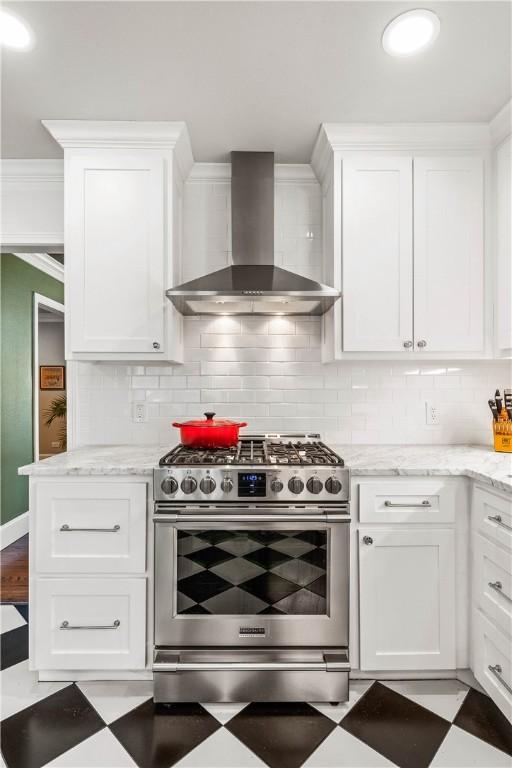 kitchen with white cabinets, ornamental molding, stainless steel stove, and wall chimney exhaust hood