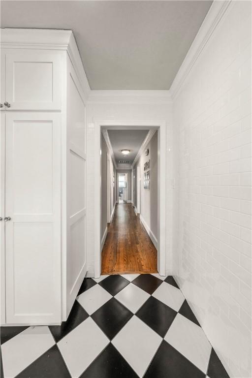 hallway with dark hardwood / wood-style flooring, crown molding, and brick wall