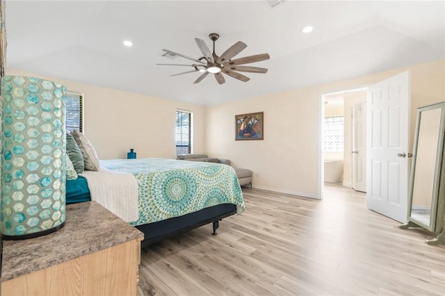 bedroom with light wood-type flooring, a raised ceiling, ceiling fan, and connected bathroom