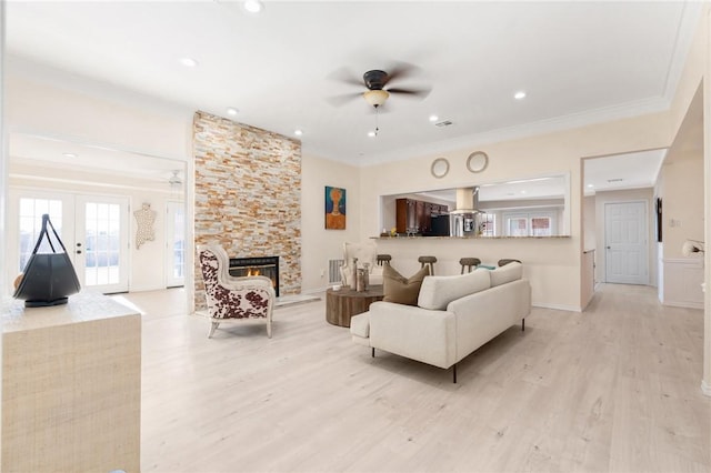 living room featuring ceiling fan, french doors, light hardwood / wood-style floors, a fireplace, and ornamental molding