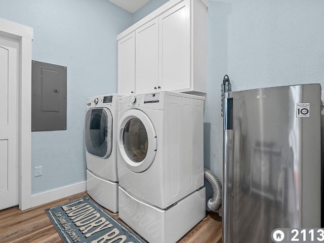 clothes washing area featuring washer and dryer, hardwood / wood-style flooring, electric panel, and cabinets