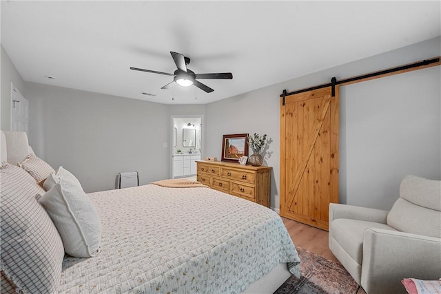 bedroom featuring a barn door, ensuite bathroom, ceiling fan, and light wood-type flooring