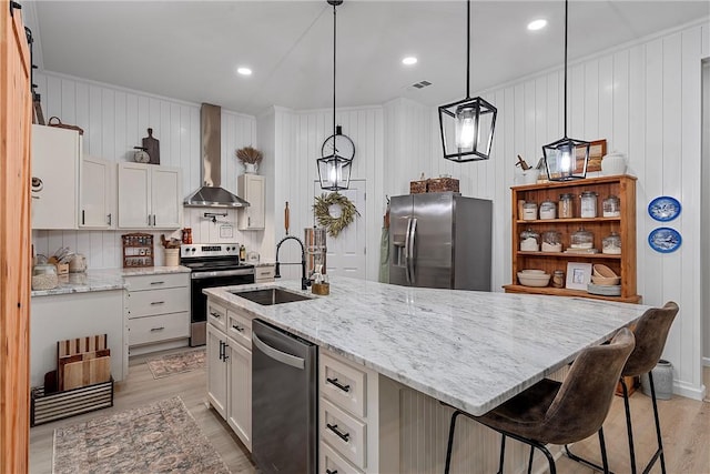 kitchen featuring white cabinetry, sink, wall chimney range hood, a center island with sink, and appliances with stainless steel finishes