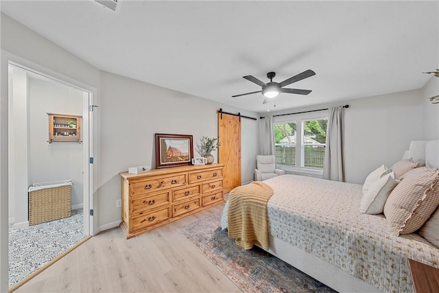 bedroom with a barn door, ceiling fan, and light hardwood / wood-style floors