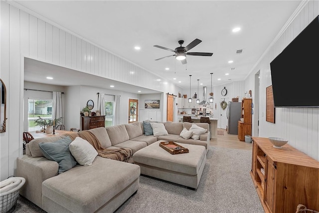 living room featuring ceiling fan, light wood-type flooring, ornamental molding, and wooden walls