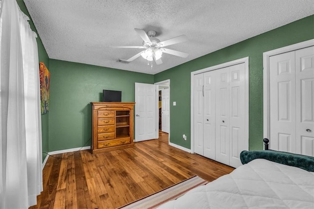 bedroom featuring two closets, ceiling fan, a textured ceiling, and hardwood / wood-style flooring