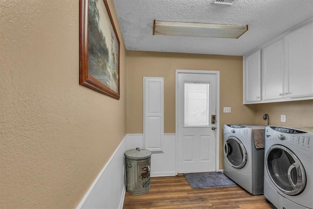 laundry room featuring cabinets, a textured ceiling, light wood-type flooring, and washing machine and clothes dryer