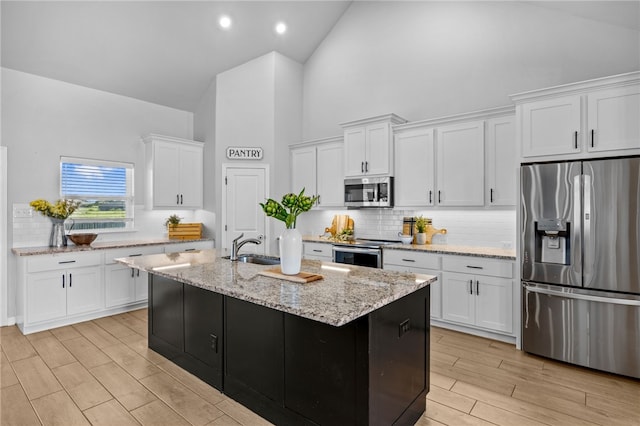 kitchen featuring wood finish floors, a center island with sink, stainless steel appliances, white cabinetry, and high vaulted ceiling