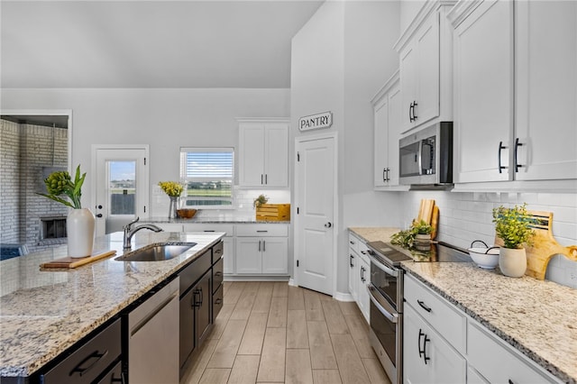 kitchen with light wood finished floors, stainless steel appliances, white cabinetry, a sink, and light stone countertops