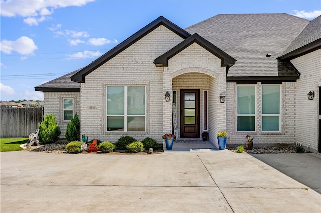 view of front of home featuring brick siding, fence, and roof with shingles