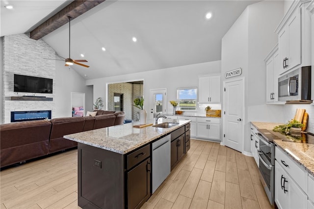 kitchen with wood finish floors, appliances with stainless steel finishes, white cabinetry, a stone fireplace, and beamed ceiling