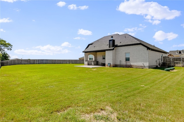 rear view of property featuring a yard, brick siding, a patio, and a fenced backyard