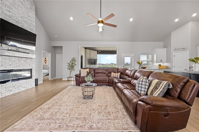 living room with light wood finished floors, recessed lighting, ceiling fan, a stone fireplace, and high vaulted ceiling