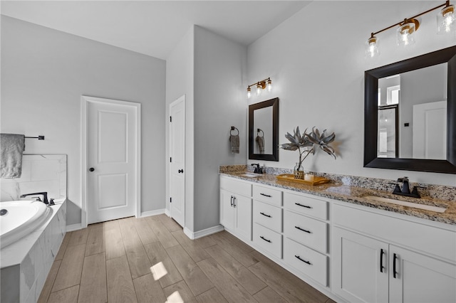 full bath featuring double vanity, a sink, a bath, and wood finished floors