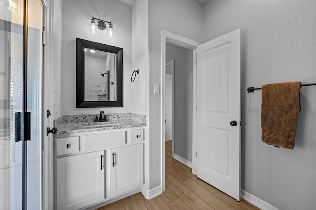 bathroom featuring walk in shower, wood finished floors, vanity, and baseboards