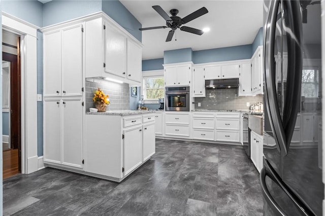 kitchen with black refrigerator, backsplash, stainless steel oven, ceiling fan, and white cabinets