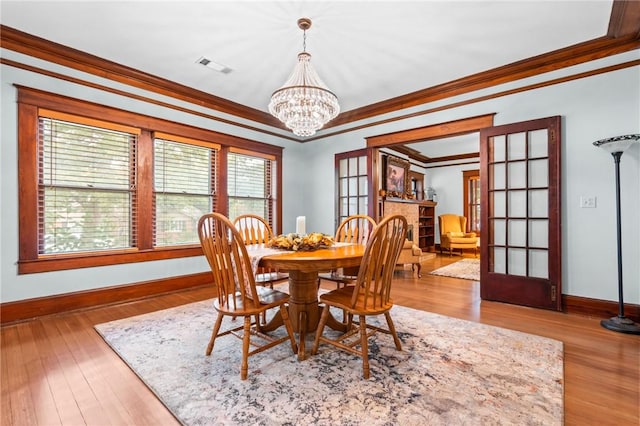 dining space with a chandelier, light hardwood / wood-style floors, crown molding, and french doors